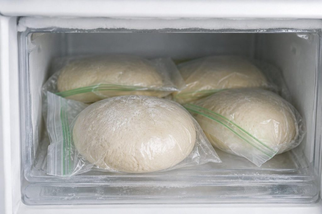Pizzadeigballer pakket individuelt i tette plastposer, plassert på en hylle inne i en fryser for langtidslagring.