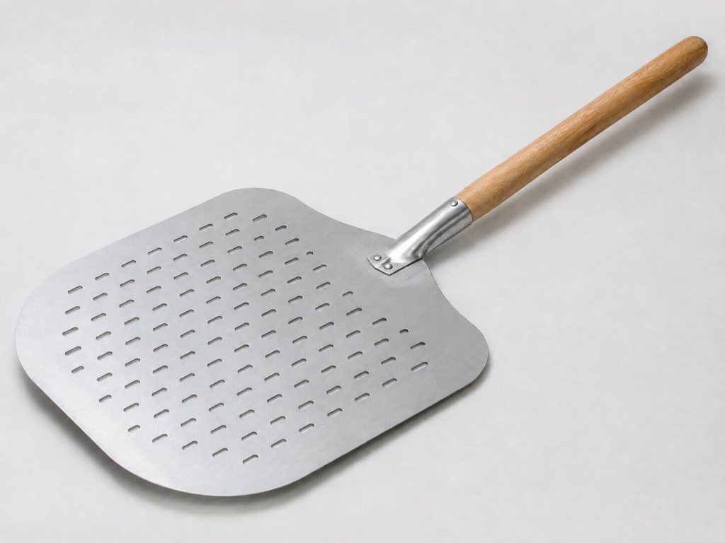 n perforert pizzaspade i aluminium med et rundt treskaft, liggende diagonalt på en lys og nøytral bakgrunn.